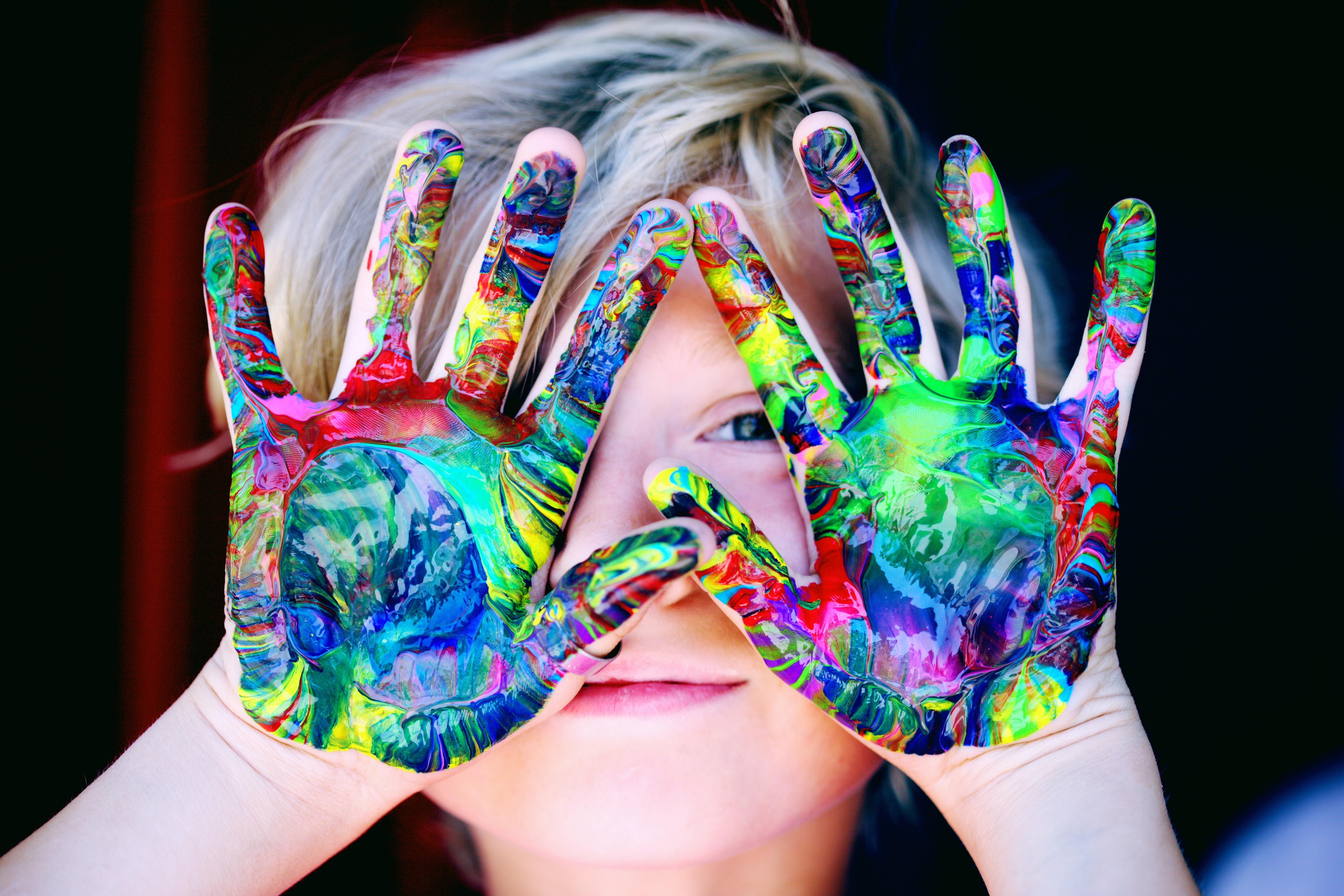 Kid hiding behind their hands with paint on them